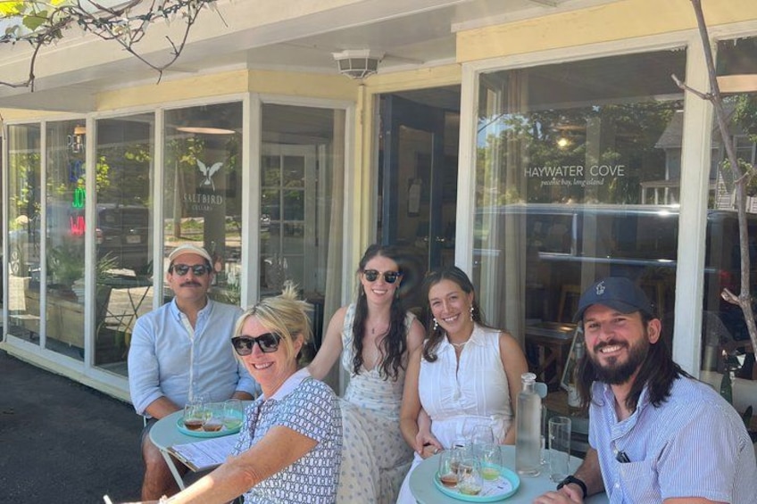 A group of people seated at tables outside a restaurant with a glass facade. 2