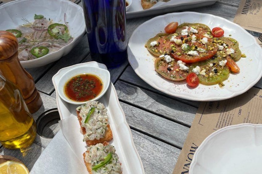 A table with various dishes, including a plate with tomatoes and feta cheese, a bowl with sliced vegetables, and a small dish with a red sauce. 3