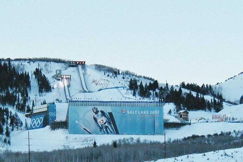 Un paysage enneigé avec une grande affiche publicitaire pour les Jeux olympiques d’hiver de Salt Lake 2002, un télésiège et une chaîne de montagnes en arrière-plan. 2