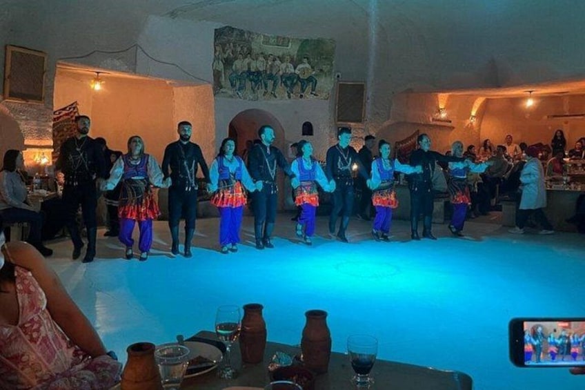 Un grupo realiza una danza tradicional en una sala tenuemente iluminada, con piso azul. 2