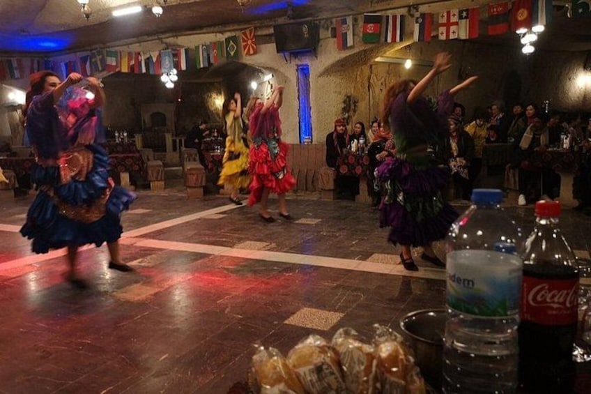 Un grupo de bailarines con trajes coloridos actuando en una sala poco iluminada con banderas colgadas en la pared. 4