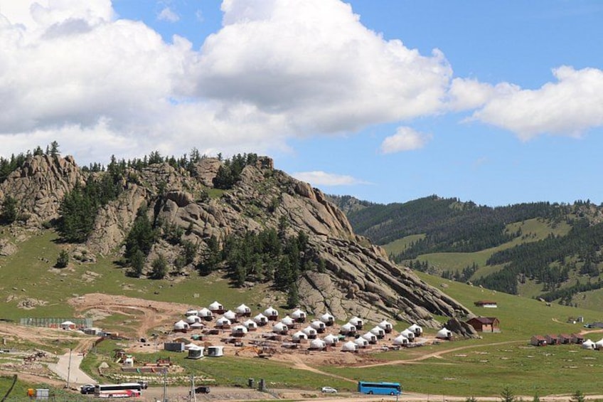 A mountainous landscape with a cluster of yurts and a rocky outcrop. 3
