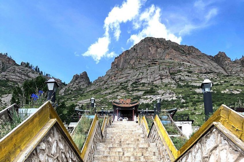 A stone staircase leading to a traditional building with a mountain backdrop. 2