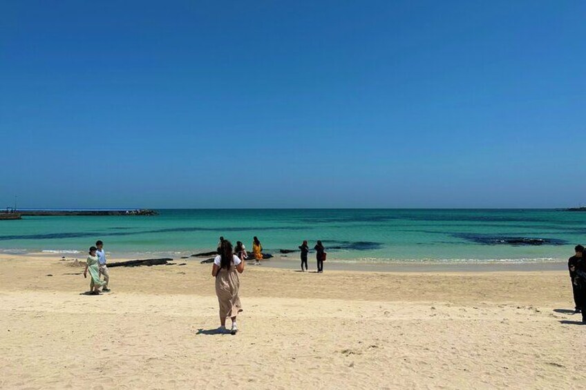 A beach with people walking and standing, a clear sky, and calm sea. 4