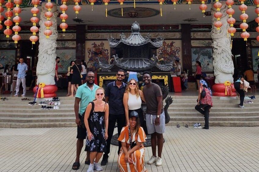 A group of people posing in front of a traditional Chinese architectural structure with ornate decorations and a dragon statue. 5
