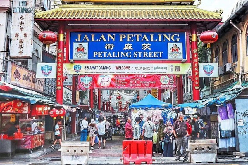 A bustling street with a prominent sign for Jalan Petaling Street, surrounded by shops and market stalls. 4