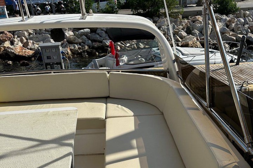 A boat's interior with a cushioned seating area, a control panel, and a rocky shoreline in the background. 2