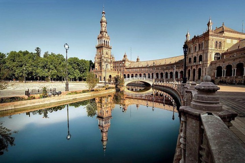 A historic building with a tower, a reflective water body, and an arched bridge. 4
