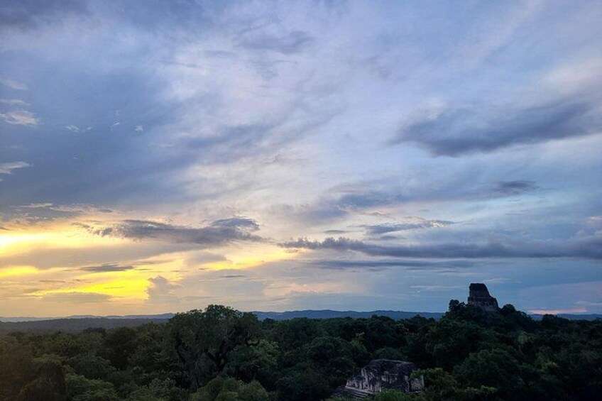 A sunset over a forested landscape with a prominent hill and a structure on top. 2