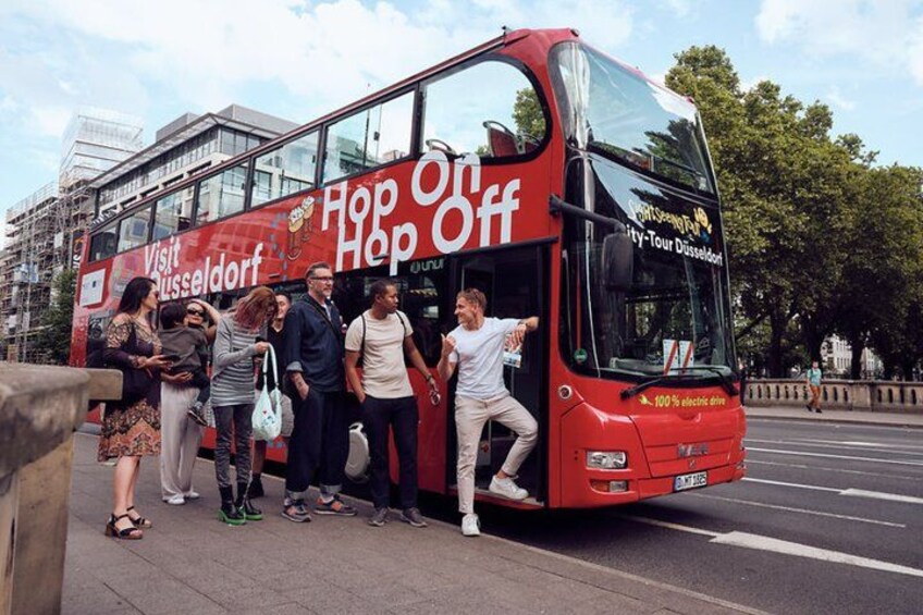 Un autobus a due piani rosso con la scritta 'Visit Düsseldorf' e 'Hop Off', parcheggiato in una strada cittadina. 4