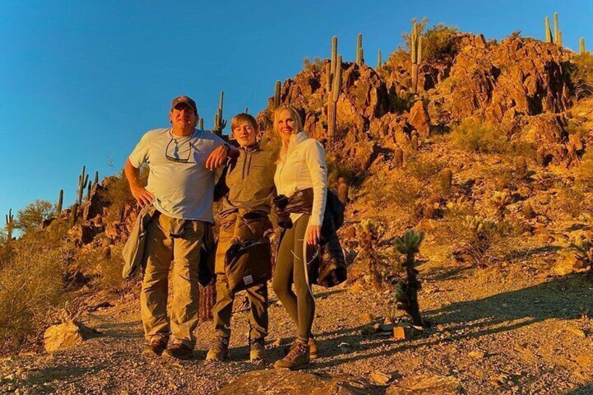 Three people standing on a rocky terrain with cacti and a clear sky. 4
