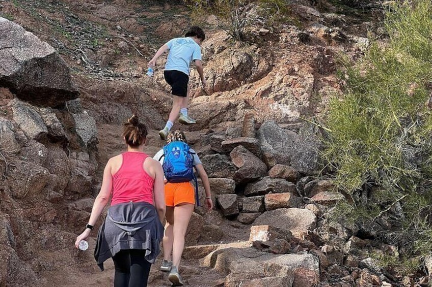 Hikers on a rocky trail with large boulders and sparse vegetation. 5