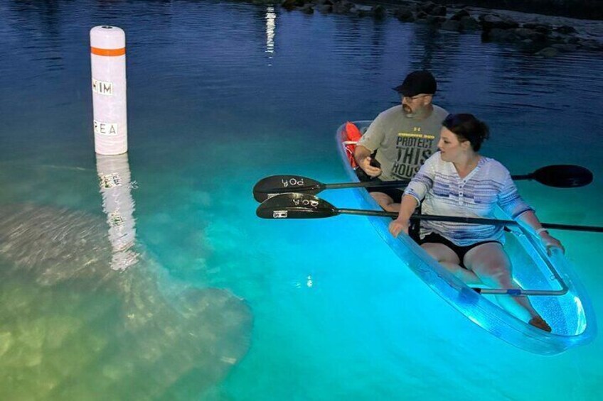 Two people kayaking on a clear blue water body with a buoy marked "NIM" and "PEA". 2
