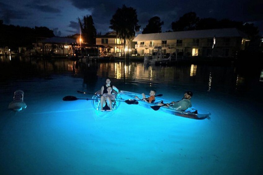 A nighttime scene with a swimming pool, people in kayaks, and a house in the background. 1