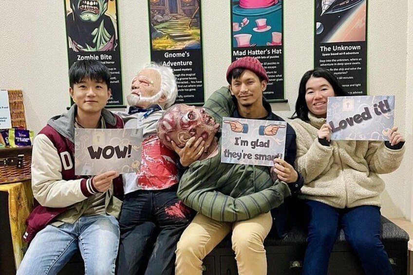 Four people holding signs with text, sitting on a bench with posters in the background. 3
