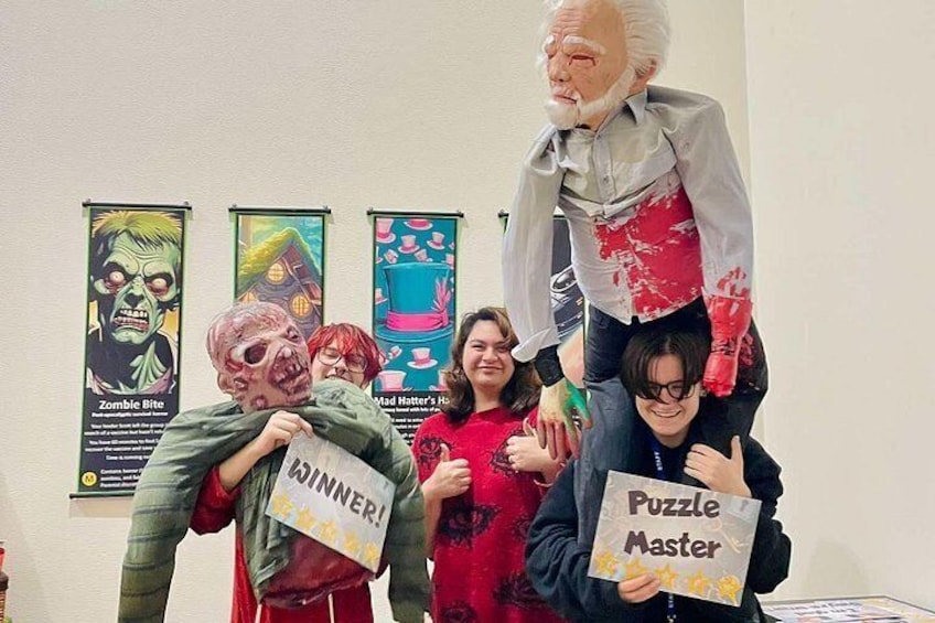 A group of people holding signs, with one sign reading 'Puzzle Master' and another 'Winner!' in a room with posters on the wall. 5