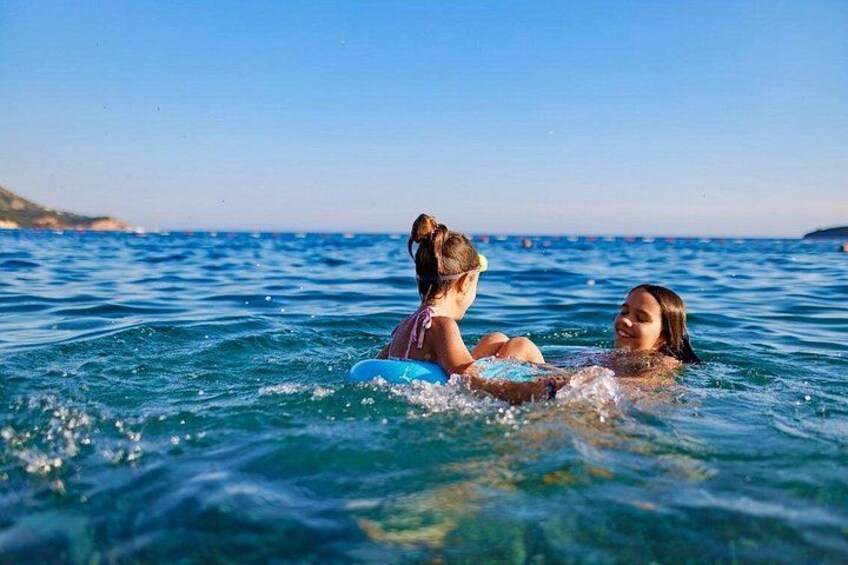 Two people floating on a body of water with a clear sky and distant land in the background. 2