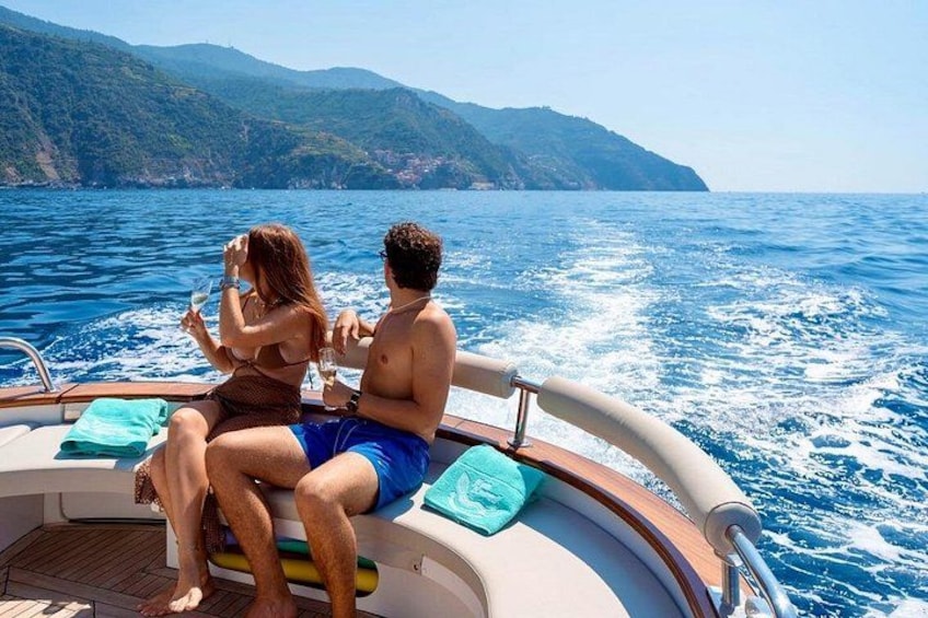 A boat with two people sitting on the deck, a mountainous coastline in the background, and the ocean. 5