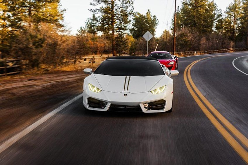 A white sports car driving on a winding road surrounded by trees. 1