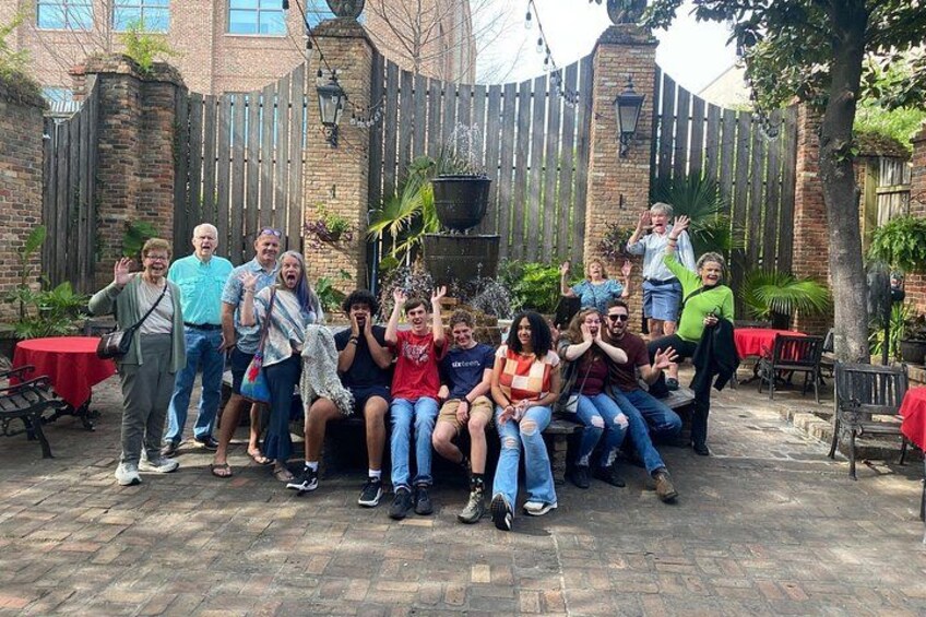 A group of people sitting and standing in a brick courtyard with a wooden fence and tables. 2