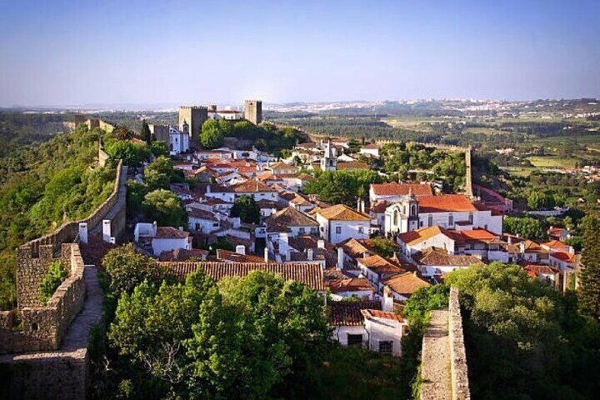 A historic town with a fortified wall, red-roofed buildings, and a prominent church. 1