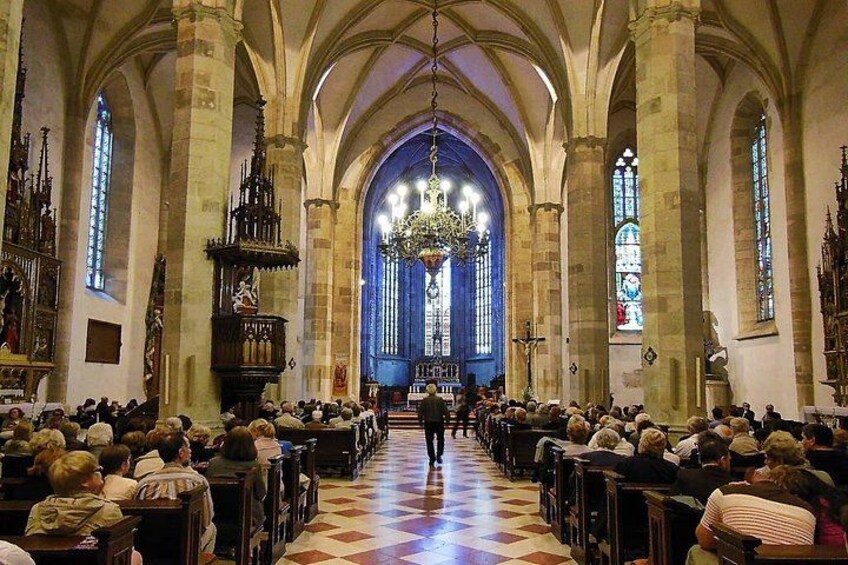 Ein Kircheninneres mit hohen Gewölbedecken, Buntglasfenstern und einem zentralen Gang. 4