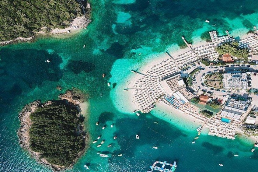 An aerial view of a coastal resort with clear turquoise waters, a sandy beach, and a marina with boats. 4
