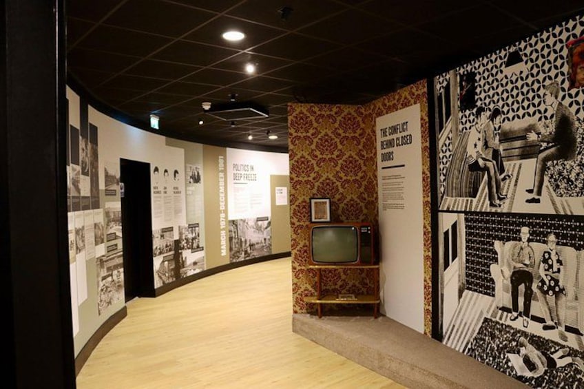 A museum corridor with historical photographs, a vintage television, and informational posters. 3