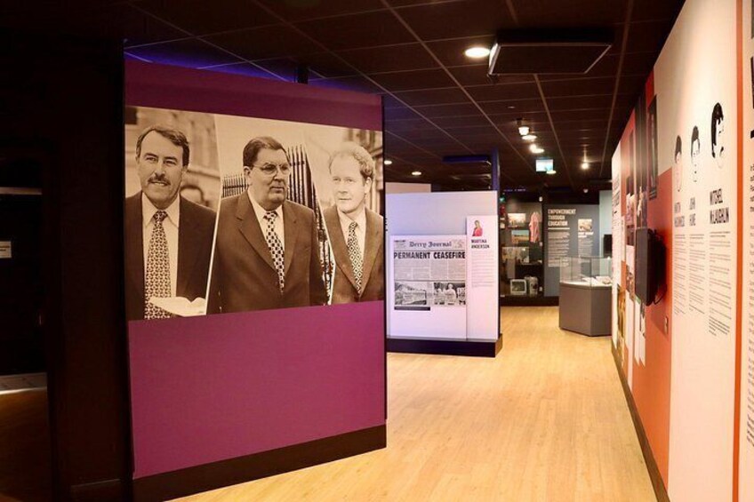 A museum exhibit with a large photograph of three men, informational panels, and a display case. 3