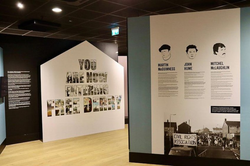 An exhibit with a large sign reading 'YOU ARE NOW ENTERING FREE DIRT' and a display of Martin McGuinness, John Hume, and Mitchel McLaughlin with their portraits and descriptions. 2