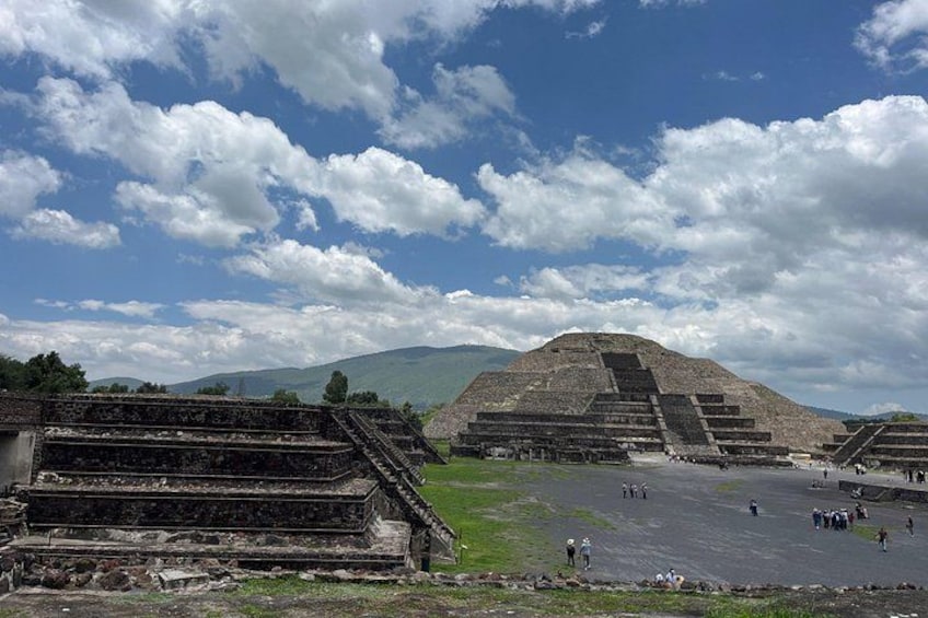 En stor pyramidekonstruktion med flere niveauer, omgivet af mindre bygninger og en klar himmel. 2