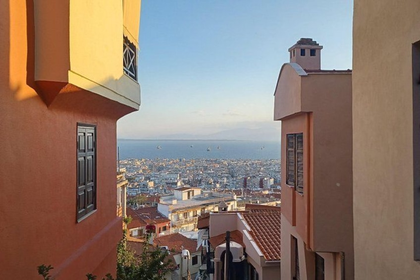 A view of a cityscape from a building with a red facade, overlooking a densely populated area with buildings and a distant coastline. 3