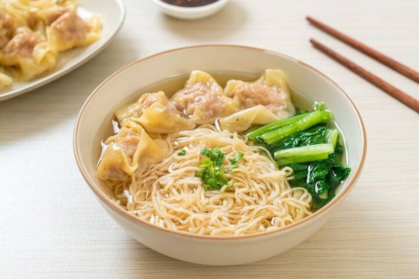 A bowl of noodle soup with dumplings and green vegetables. 1
