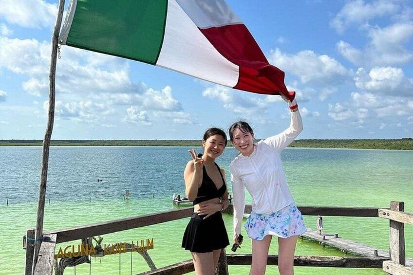 Two people on a wooden dock with a clear view of a turquoise sea and distant land. 2