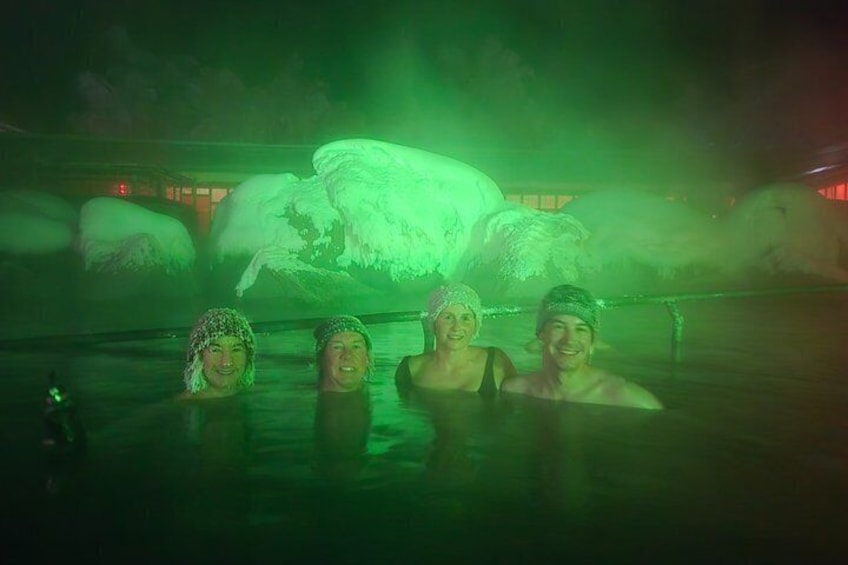 A group of people in a hot spring with a large, feathered sculpture in the background. 4