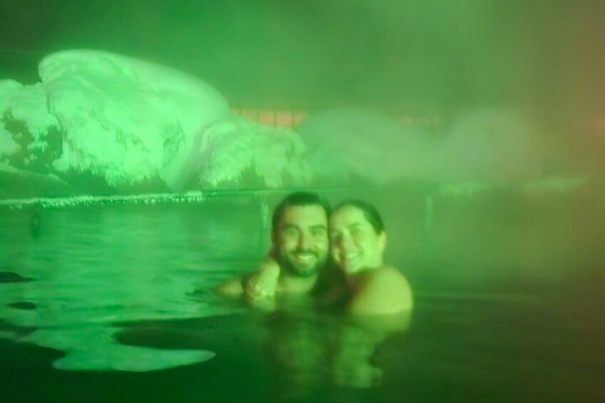 Two people in a green-lit pool with a large ice formation in the background. 3
