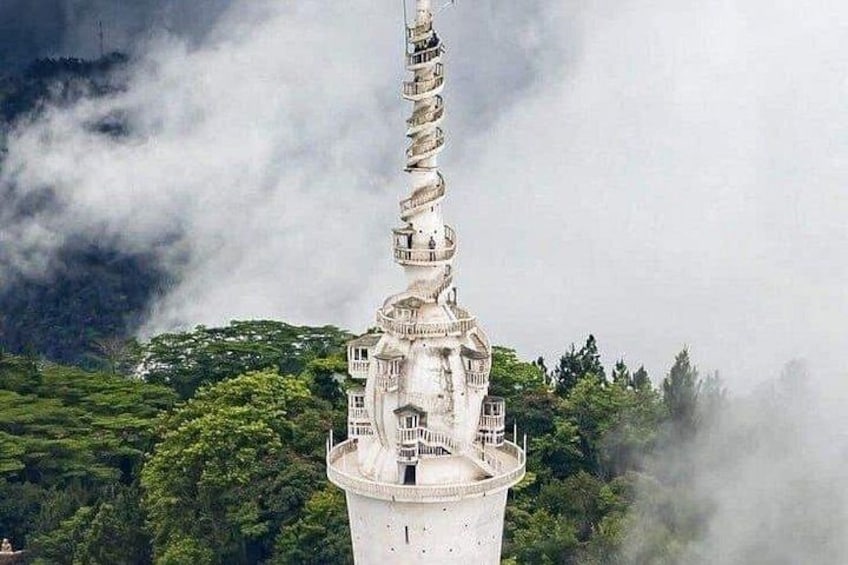 A tower with a spiral staircase, surrounded by lush greenery and mist. 1