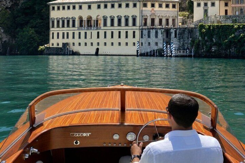 A wooden boat with a man steering, water, and a building in the background. 4