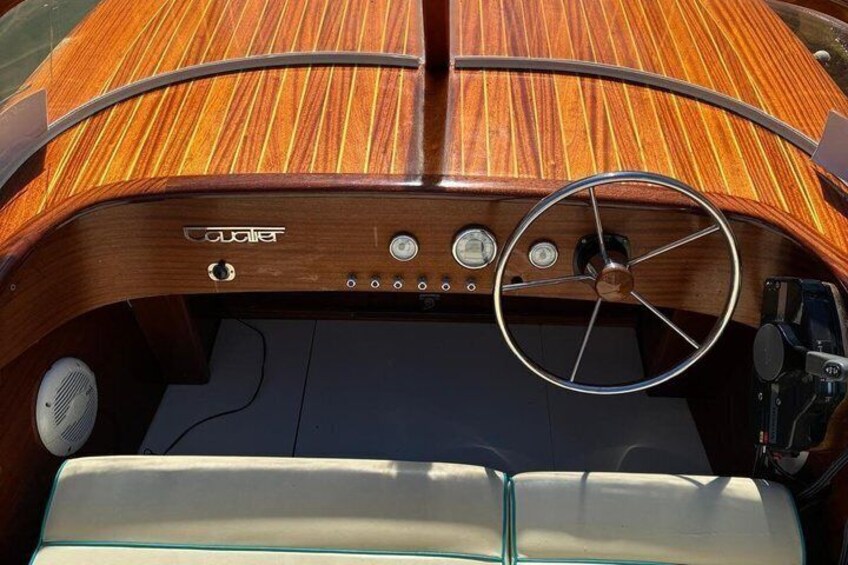 A wooden boat interior with a steering wheel, control panel, and seating area. 2