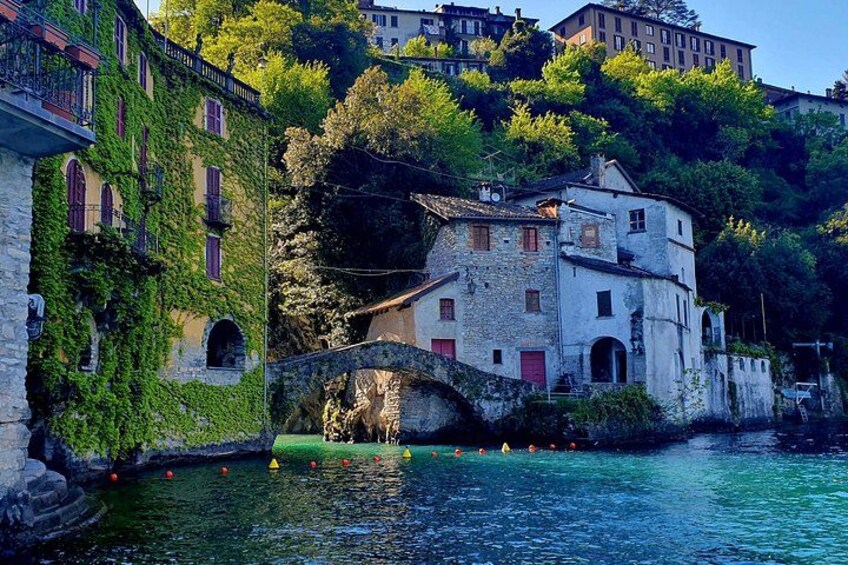 A stone bridge over a river, surrounded by buildings with ivy-covered walls and a hilltop building in the background. 3