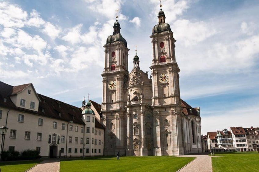 A historic church with two prominent towers, a well-maintained lawn, and surrounding buildings. 1