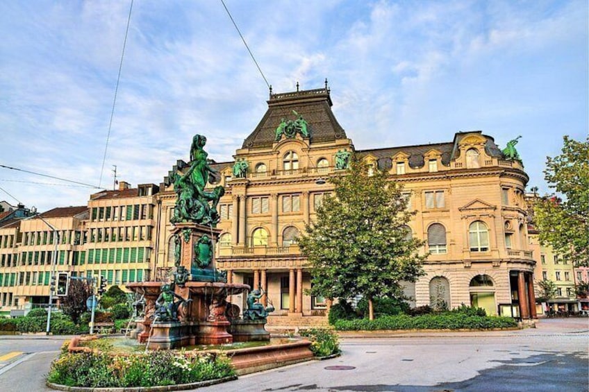 A historic building with ornate architecture, a fountain with statues, and a clear sky. 2