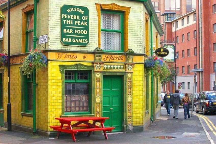 A yellow and green pub named 'Wilson's Peever of the Peak' with a green door and a red bench outside. 1