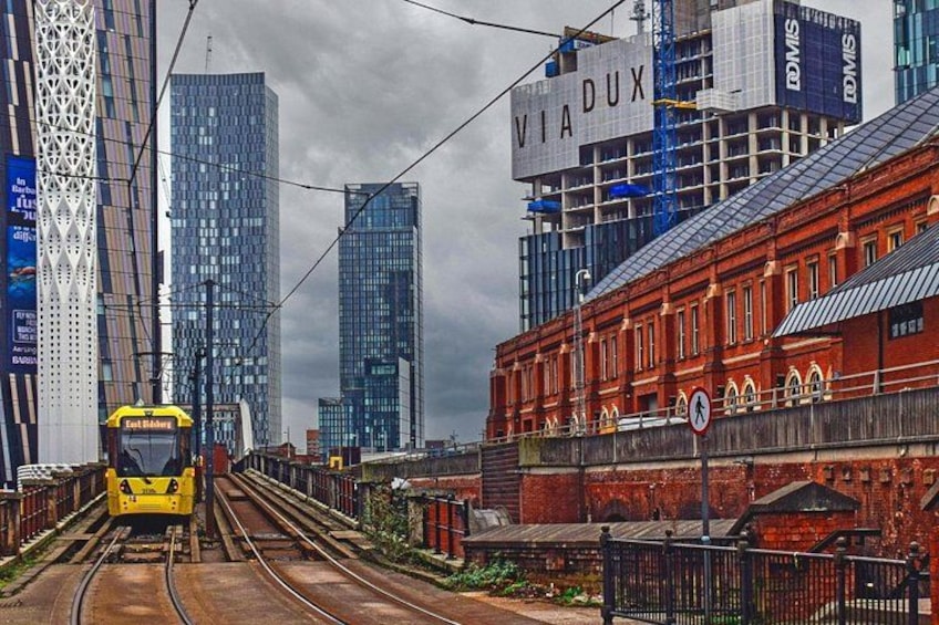 A yellow tram on tracks, a red brick building, and modern high-rise buildings in the background. 2