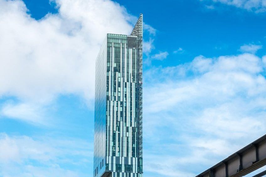 A tall, modern skyscraper with a glass facade and a pointed top, set against a blue sky with scattered clouds. 3