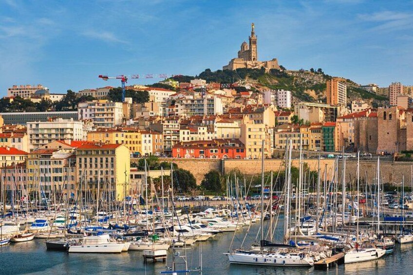 Un port où sont amarrés de nombreux voiliers, un bâtiment historique perché sur une colline et, au loin, une vue sur la ville. 1