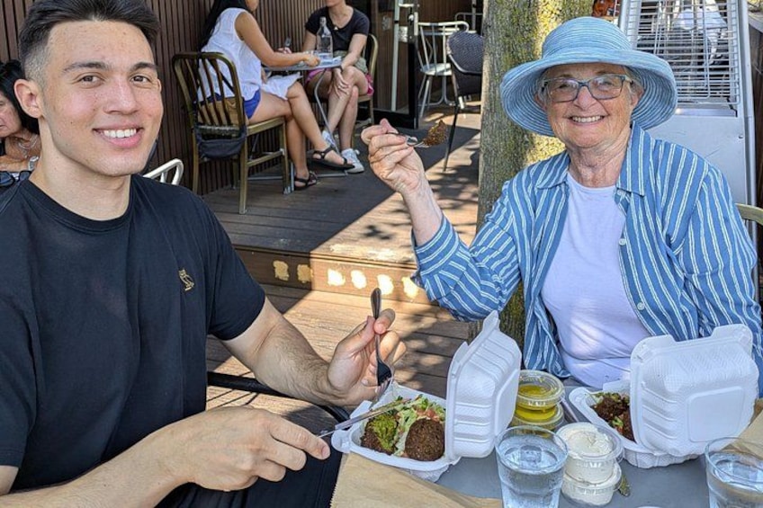 Two people dining outdoors with food and drinks on a table. 3