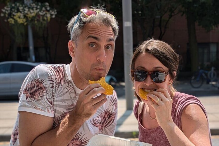 Two people sitting at a table outdoors, eating snacks. 3