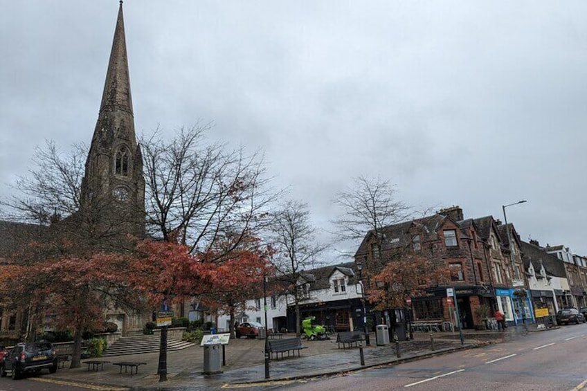 A church steeple, a red-leaved tree, and a street with buildings. 5