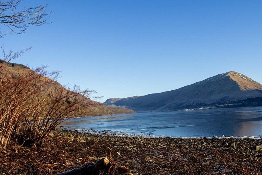 Un lac avec une montagne en arrière-plan et des arbres sans feuilles le long de la rive. 2